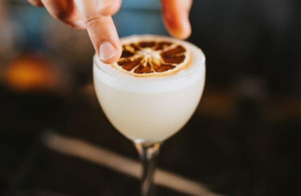 A pino colada white cocktail with a bartender putting dried fruit on top
