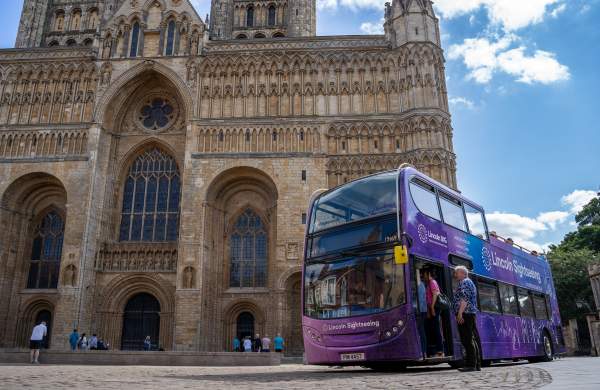 Lincoln Sightseeing bus outside Lincoln Cathedral in sunlight with people waiting to board.