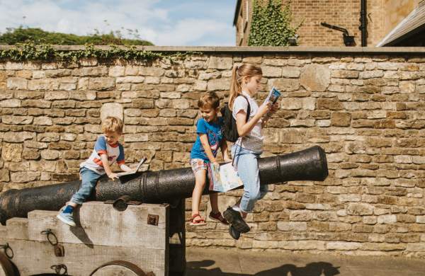 Three children sat on a castle cannon examining a guidebook