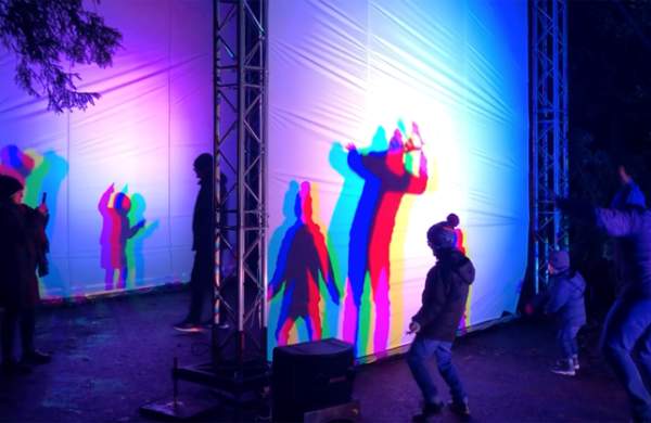 A light installation with children dancing in front and creating shadows