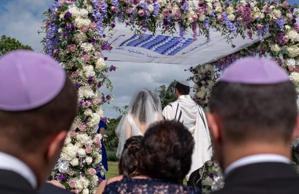 Jewish couple in a wedding ceremony under a floral chuppah wedding canopy.