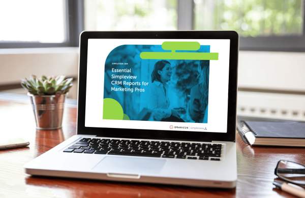 The Essential Simpleview CRM Reports for Marketing Pros guide open on a laptop that's sitting on a desk.