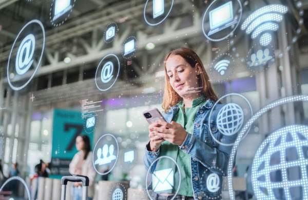Traveler using a smartphone in a transit hub, surrounded by digital communication and connectivity icons representing smart travel technology.