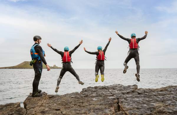 Group of people coasteering and jumping into water while instructor watches on
