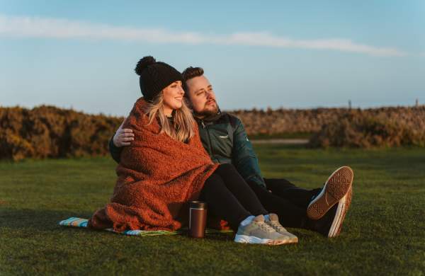 Young couple under a blanket with a coffee watching a sunset at rhossili bay in the winter