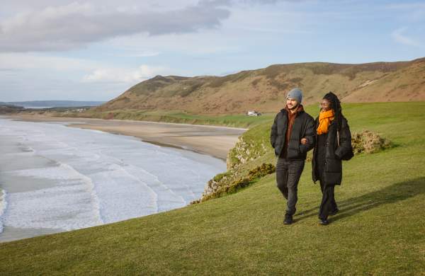 Couple walking along rhossili bay coastline