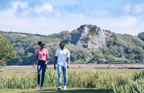 A man and a woman walking at Whitford with craggy rocks in the background.