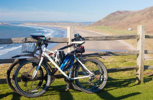 Bikes against a fence with Rhossili Bay in the background.