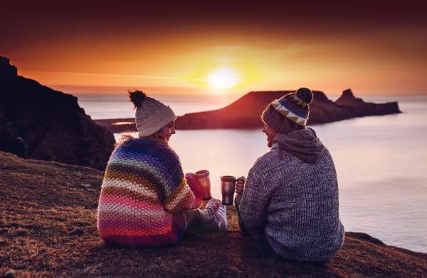 a couple share coffee while the sun sets against worms head
