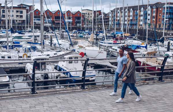 A man and woman walking around Swansea Marina.