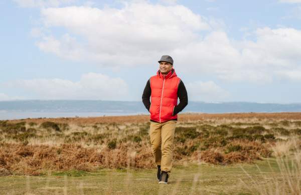 A man in a bright red bodywarmer and flat cap walking on Gower.