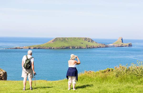 An older couple at Rhossili looking out to Worm's Head. The woman is using binoculars.