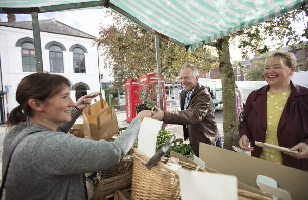 a man and woman stood at a market stall purchasing fruit and vegetables