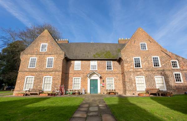 A thatched manor house with gardens and gates from the front