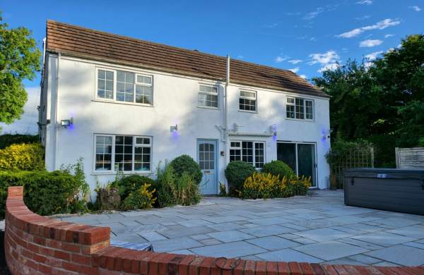 a white cottage from outside with brick wall surrounded by bushes