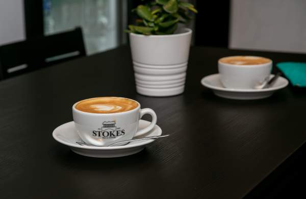 Stokes coffee mug with coffee on table with plant in background