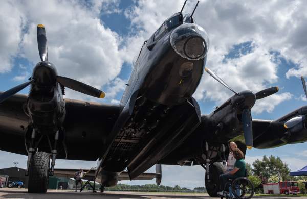 A man and a woman stand beneath a Lancaster Bomber Plane at an aviation heritage centre