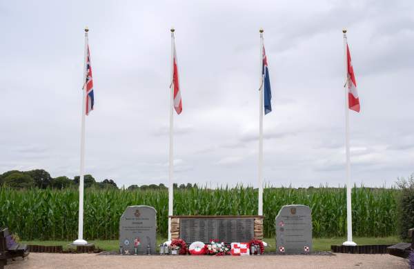 flags in front of a wall memorial with grass and cloudy skies