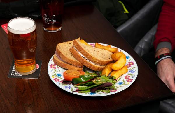 a beer and a sandwich on a plate in a pub with chips
