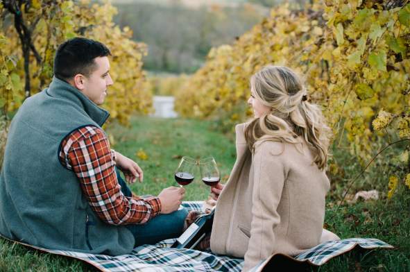Couple drinking wine while sitting on the ground between in the vines of Bluemont Vineyard