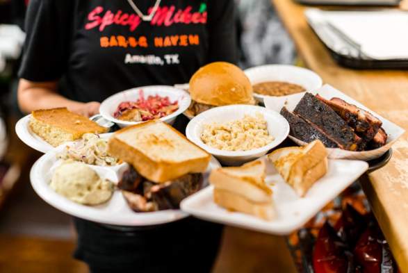 multiple different dishes of texan barbeque being served by a waitress