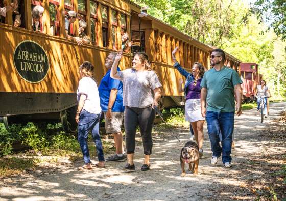 People enjoying a beautiful day walking alongside the steam engine on the heritage rail trail