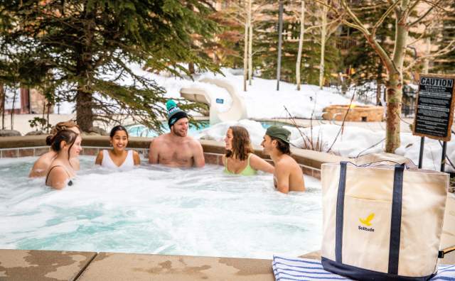 6 people in a hot tub with snow on the ground and pine trees around them