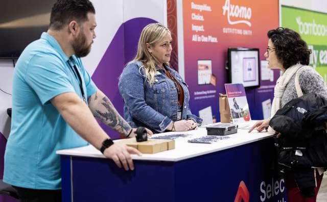 3 people standing at a tradeshow booth talking