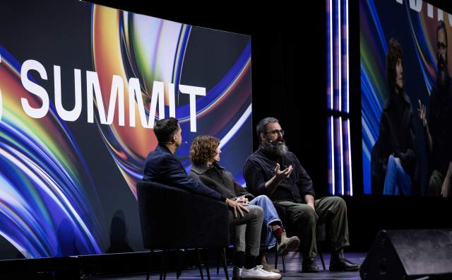 Jared and Jerusha Hess seated addressing a crowd with a moderator the background has the summit logo