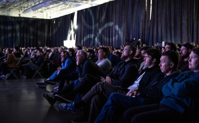 Crowd of people in seats looking attentively toward a stage that is out of the picture