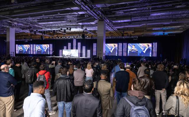 People standing at the back of a convention speaking room because there are not enough seats