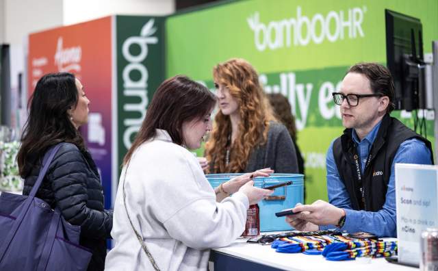 woman holding a phone talking to a man standing in front of a brightly colored background that says bambooHR
