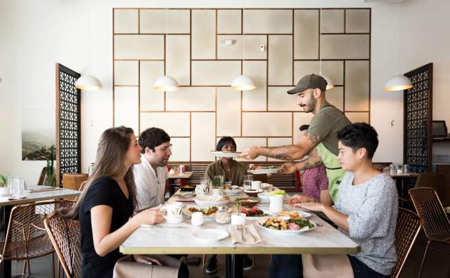 Man Serving Food To 3 People At A Table In Laziz Kitchen