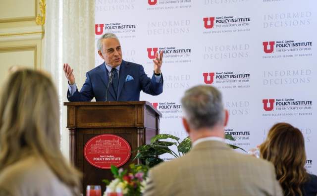 Man in business suit speaking at a podium the backdrop behind him has University of Utah Policy Institute