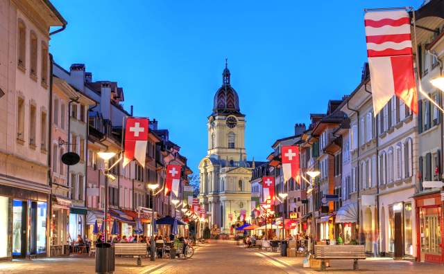 View of Temple De Morges down a street at twilight with swiss flags and blue sky