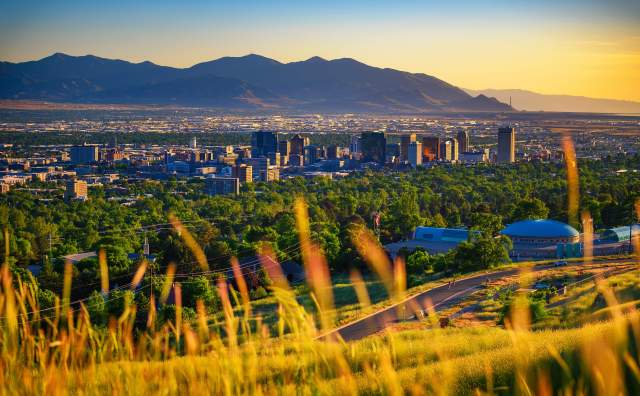 Scenic view of Salt Lake with wild summer grass in the foreground then green trees, then the city  with the mountains and golden light in the background