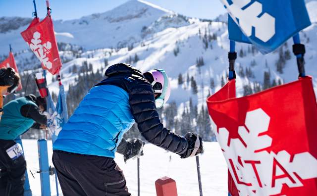 Skier at a racing start line that is marked with Alta flags with mountains in the background