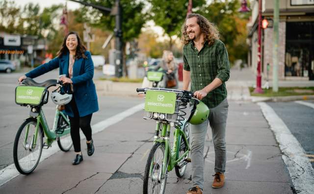 Two people walking GREENbike's around the 9th and 9th location of Salt Lake.