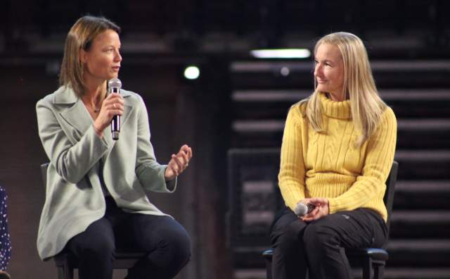 2 women sitting on a stage talking to each other