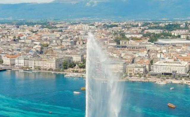 Aerial view of the fountain on Geneva lake making a rainbow in the mist with the city and then the mountains in the background