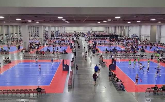 Indoor volleyball courts in a convention hall. Players are at each court with spectators