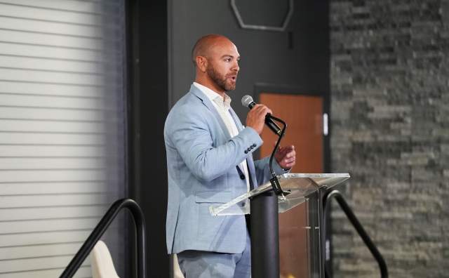 Bald man with beard in  light blue suit standing at a podium speaking