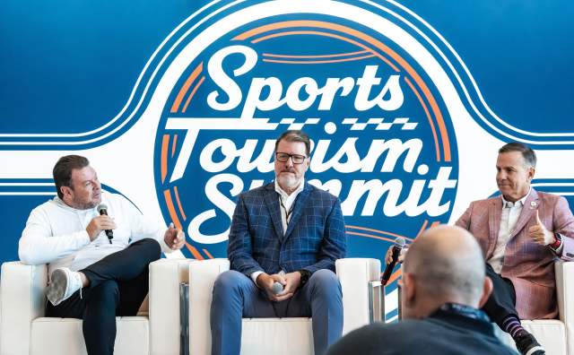 Background says Sports Tourism Summit with 3 men in suits sitting in white chairs in front of it
