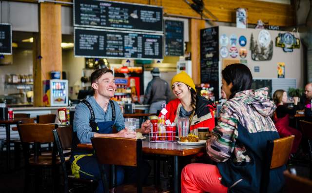 A group of people sitting at a table with food. The menu and serving counter are behind them