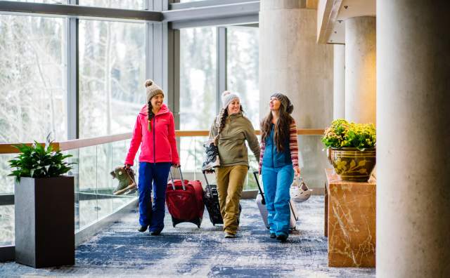3 women in ski gear pulling suitcases in the atrium area of the Cliff Lodge