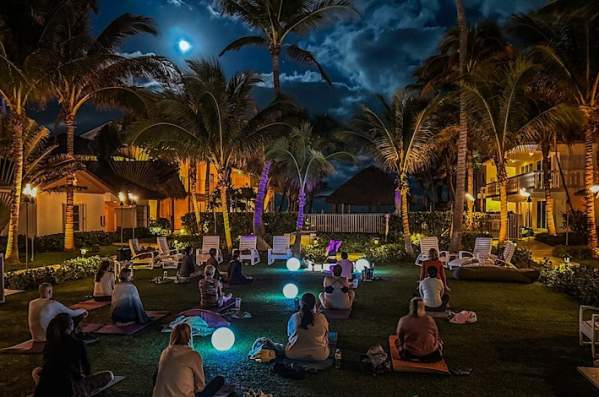 A groupmeditating under a full moon in a grassy courtyard at the Beachcomber Resort and Club. Colorful orbs are interspersed throughout the group