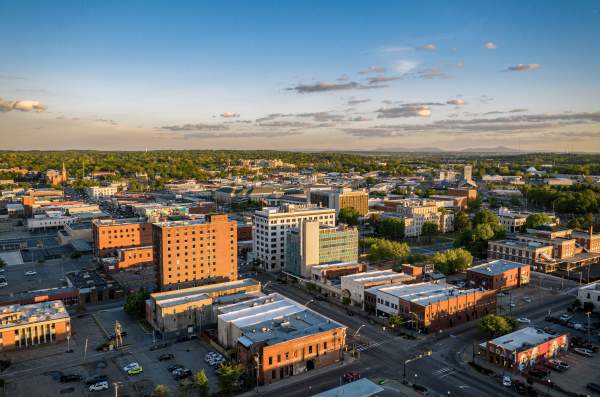 The city of Fort Smith is covered in the light of sunset. Green, lush hills are visible behind downtown buildings.