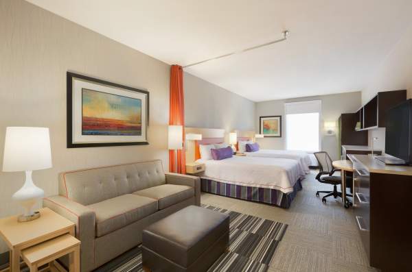 A hotel room with two queen beds, a couch, large work space, and TV is ready to welcome you in Fort Smith.