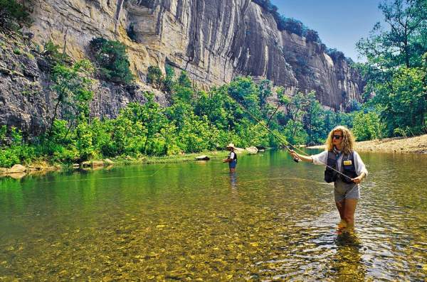 Two people stand knee deep in water as they fly fish in the Buffalo River in Arkansas.