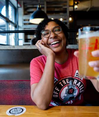 A young Black woman cheerses a beer to the camera at Lone Girl brewing Company